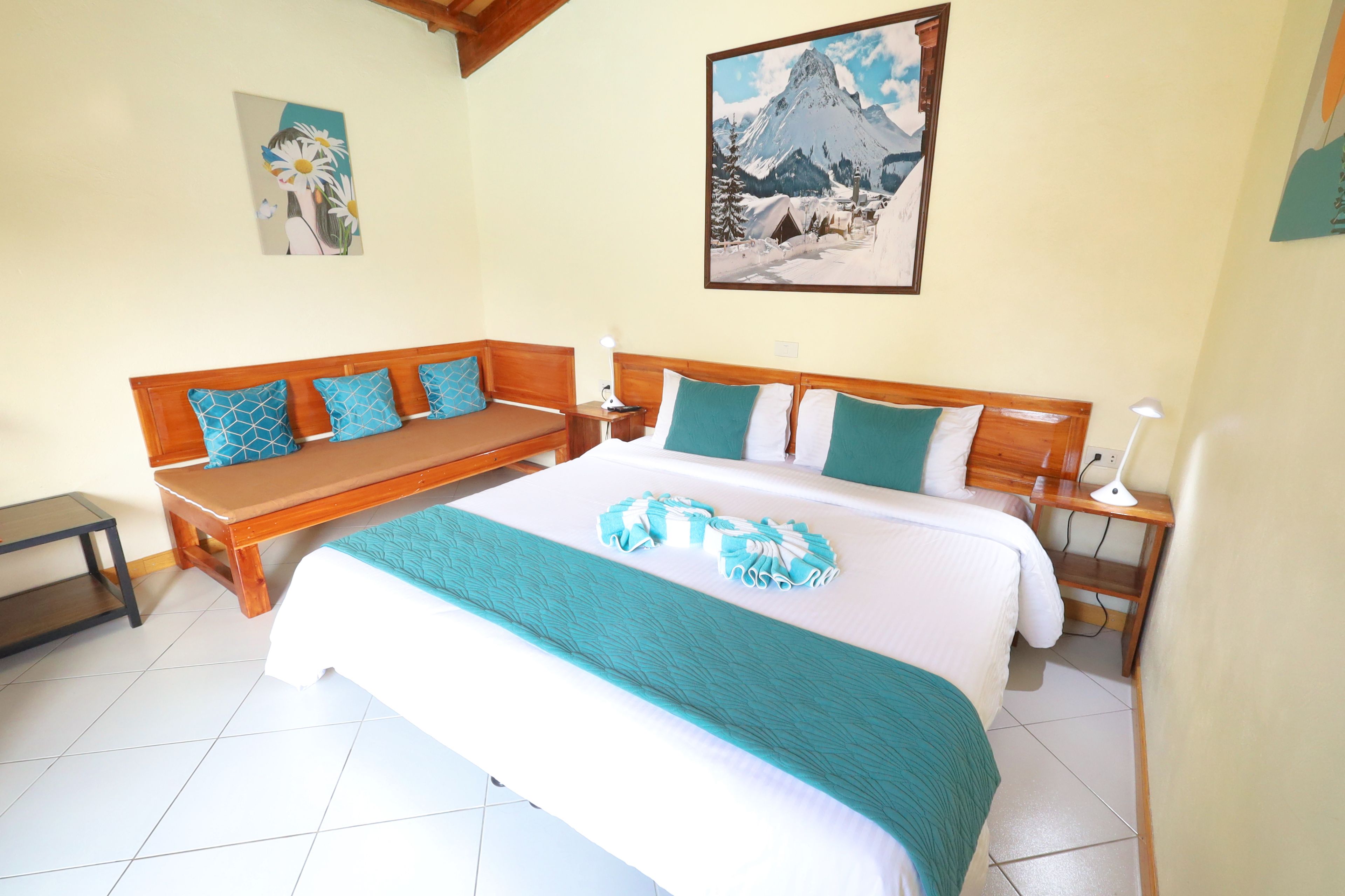 A bedroom with a bed, a wooden bench, a nightstand, and two paintings on the wall.