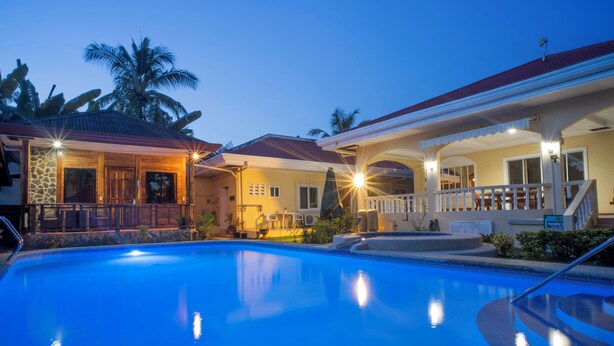 A swimming pool with a covered area, a stone facade building, and a palm tree in the background. - Alona Austria Resort (Panglao)