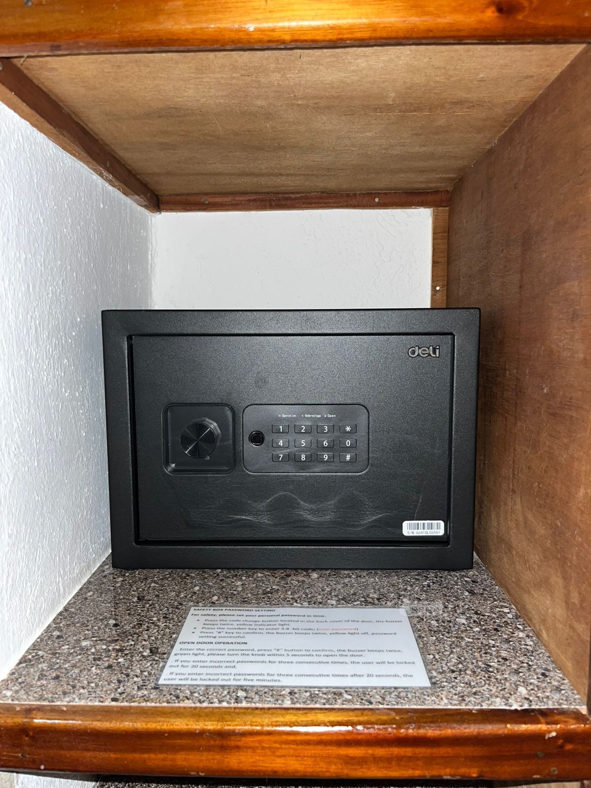A black safe with a keypad and a dial lock, placed in a wooden cabinet with a granite countertop.