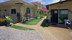 A yellow building with a red roof, a reception area, and a well-maintained garden with various plants and a gravel pathway. - Alona Austria Resort (Panglao)