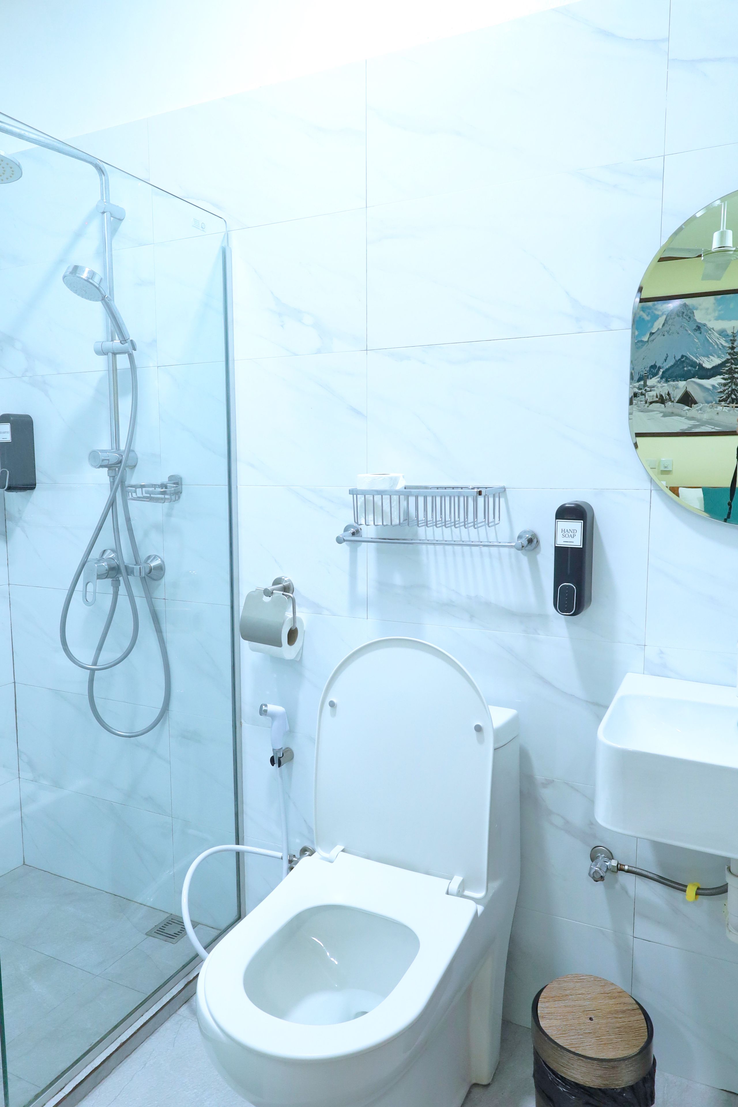 Een badkamer met een douche met glazen wand, een toilet, een wastafel en een zeepdispenser.