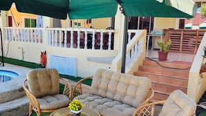 An outdoor seating area with wicker furniture, a round table, and a green umbrella. - Alona Austria Resort (Panglao)