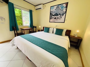 Una habitación de hotel con cama, escritorio, silla, mesita de noche, lámpara y ventana con cortinas.