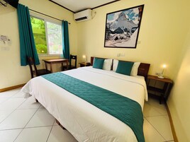 Una habitación de hotel con cama, escritorio, silla, mesita de noche, lámpara y ventana con cortinas.
