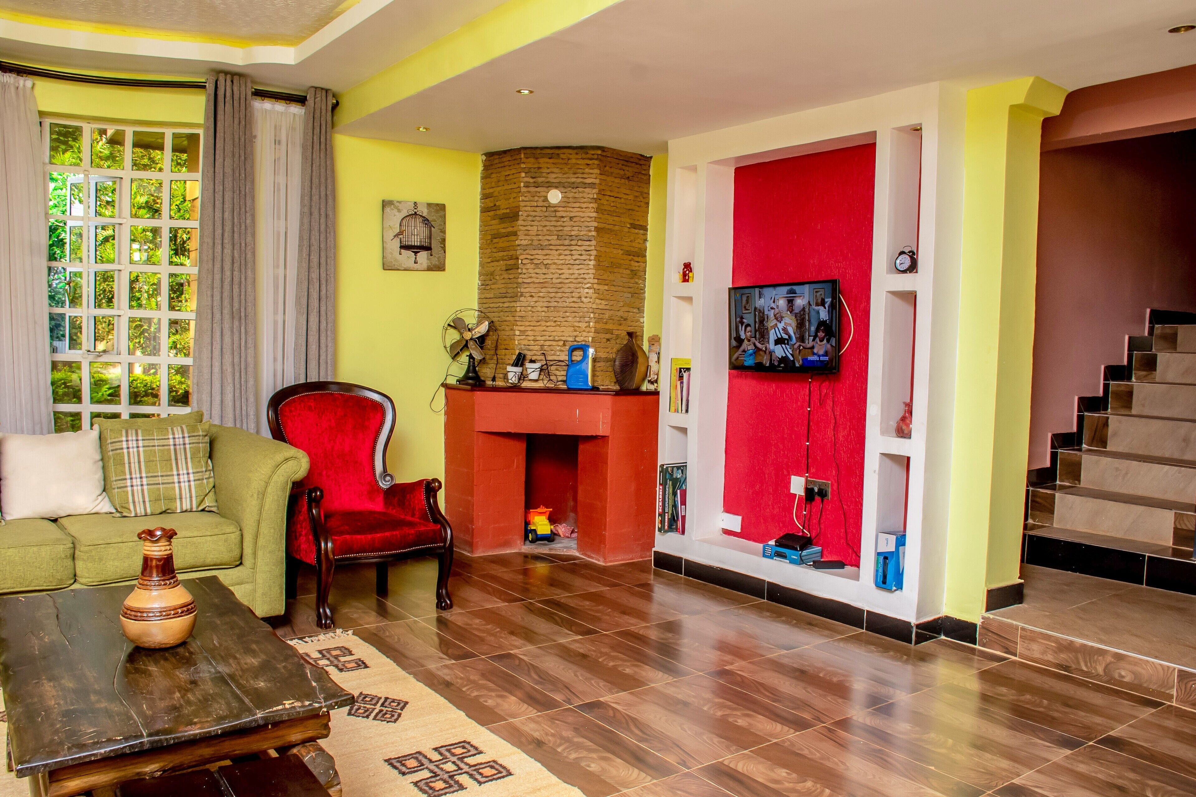 A living room with a green sofa, a red armchair, a fireplace, a television, and a staircase.