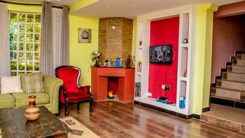 A living room with a green sofa, a red armchair, a fireplace, a television, and a staircase.