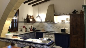 A kitchen with a central island, a stove, and a microwave. There is a hanging light fixture and a wooden cabinet.