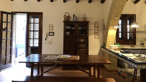 A dining area with a wooden table, a cabinet with glass doors, and a tiled backsplash in the kitchen area.