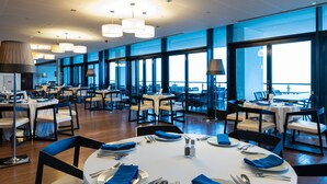 Un vaste espace dédié à la salle à manger, avec de nombreuses tables dressées, de grandes fenêtres offrant une vue dégagée et un éclairage moderne.