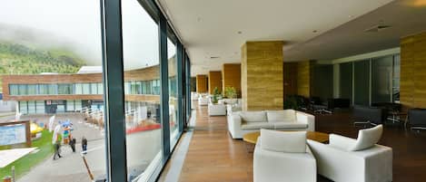A spacious lobby with modern furniture, large windows, and a view of a building with a green landscape.