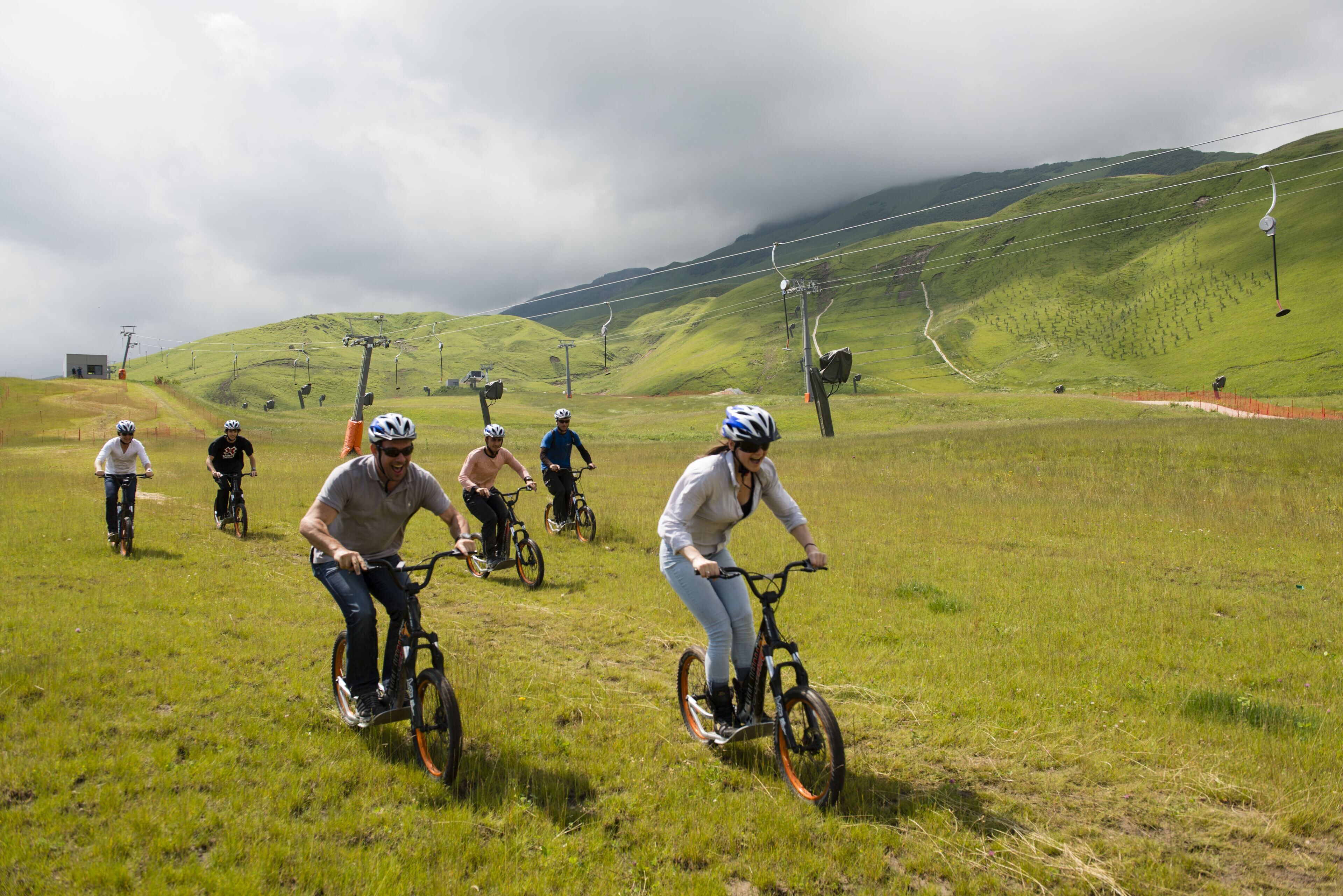 A group of people riding bicycles on a grassy hill with a ski lift in the background.