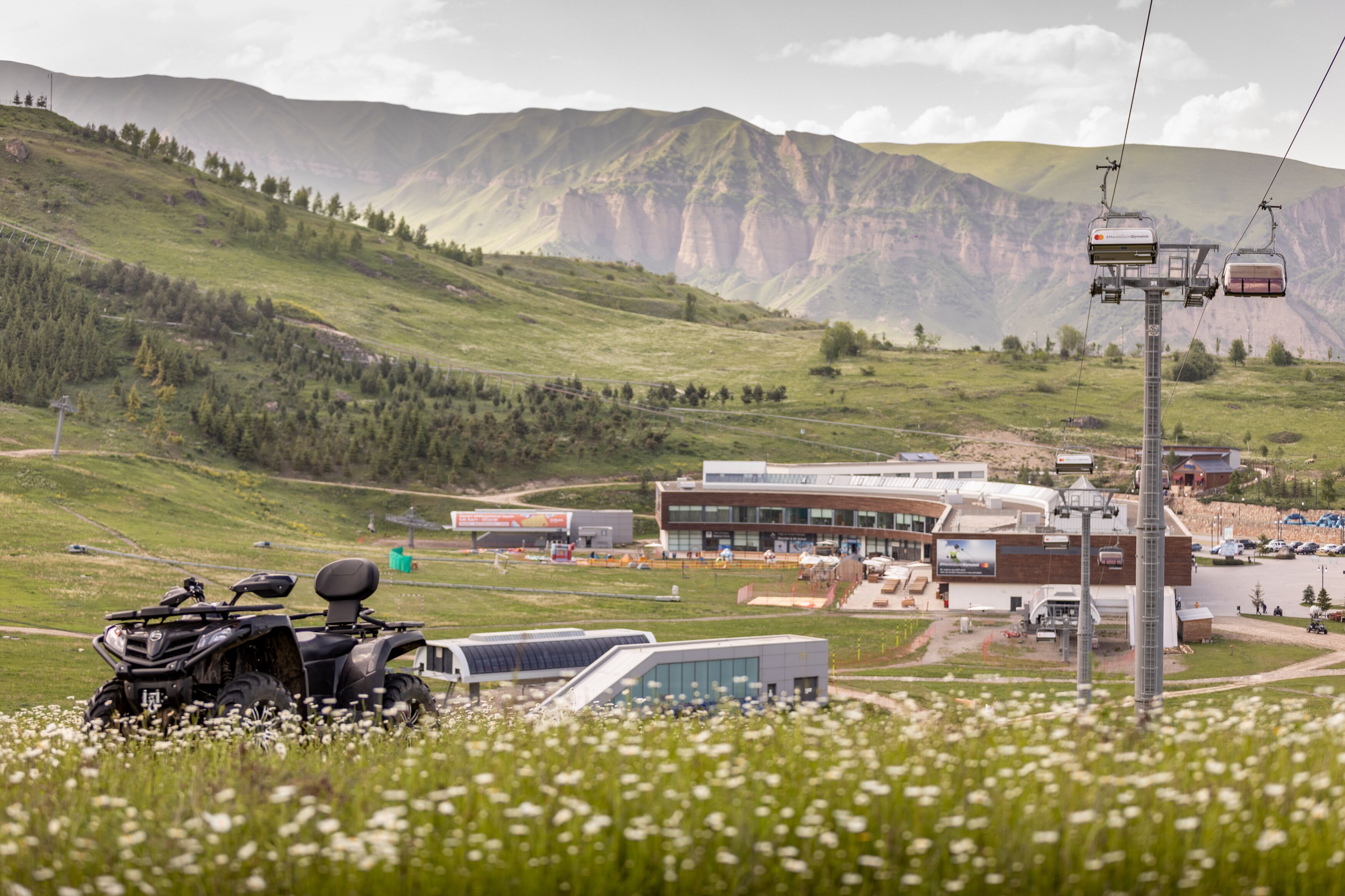 A modern building with a flat roof and large windows, surrounded by a green landscape with mountains in the background.