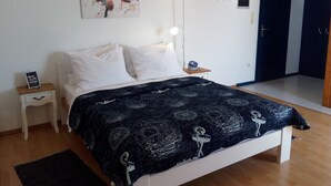 Une chambre à coucher comprenant un lit, une table de chevet, une lampe, un tableau ou une décoration murale, et une porte.