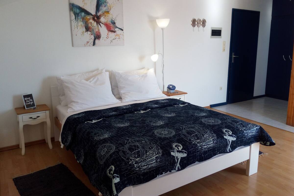 A bedroom with a bed, a nightstand, a lamp, a wall art piece, and a door.