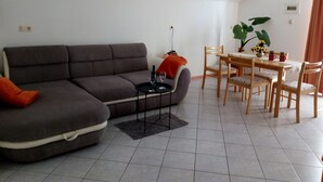 Un salon avec un canapé gris, une petite table ronde sur laquelle se trouve un verre à vin, et un coin repas avec une table et des chaises en bois.