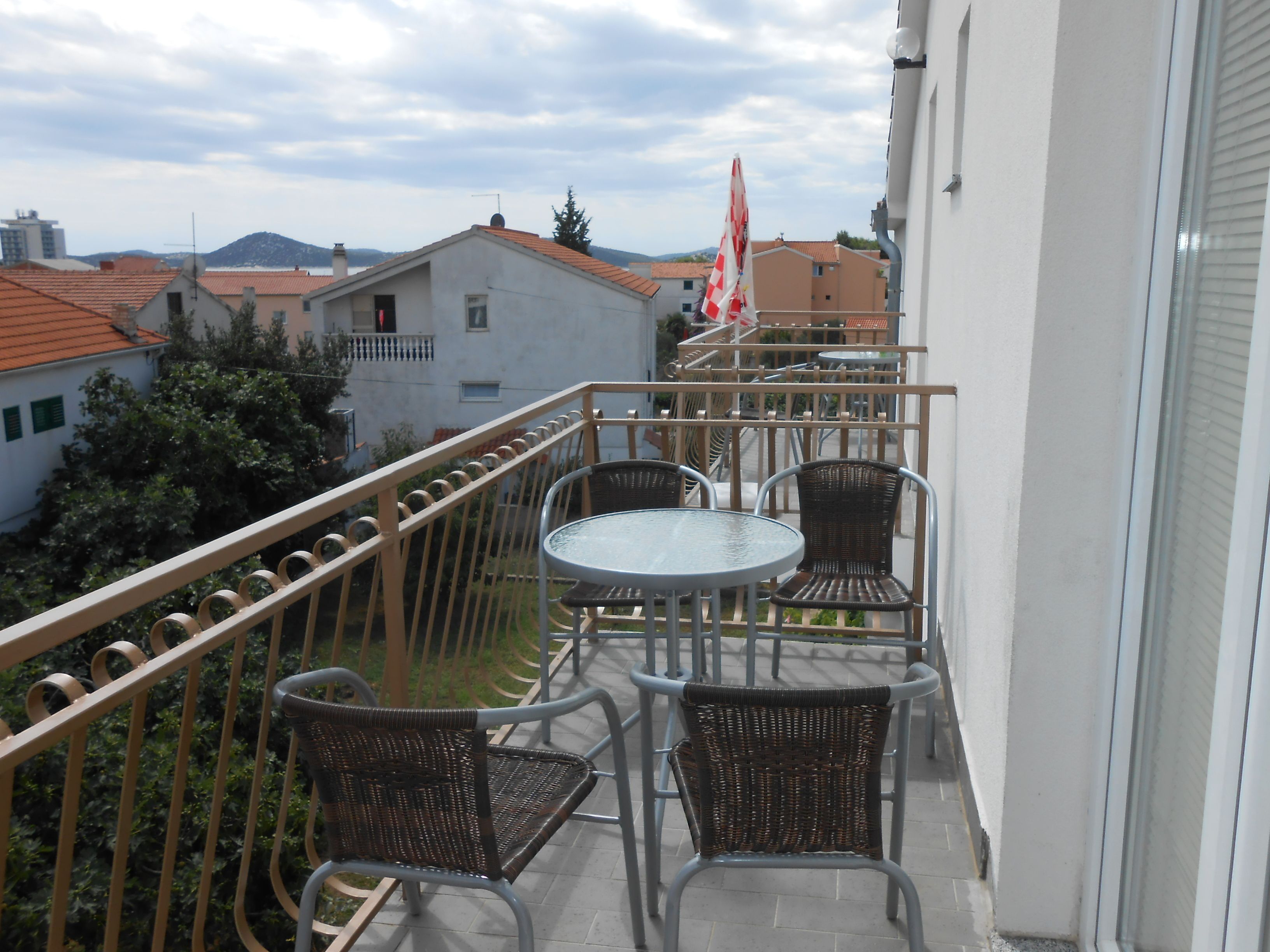 Un balcone con un tavolo e quattro sedie in vimini, affaccia su una città con edifici e una montagna all'orizzonte.