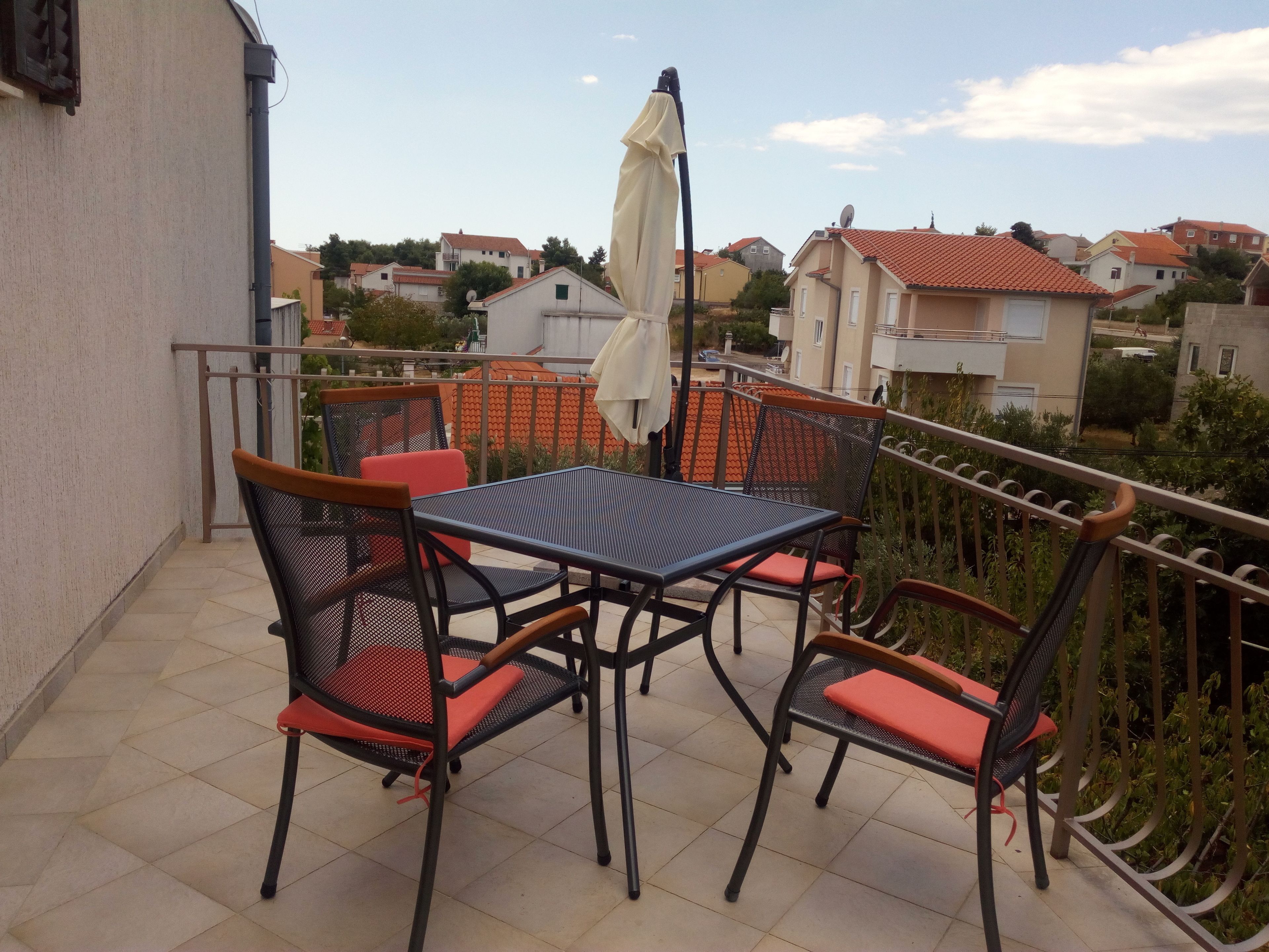 A balcony with a table and chairs, a railing, and a view of neighboring houses.