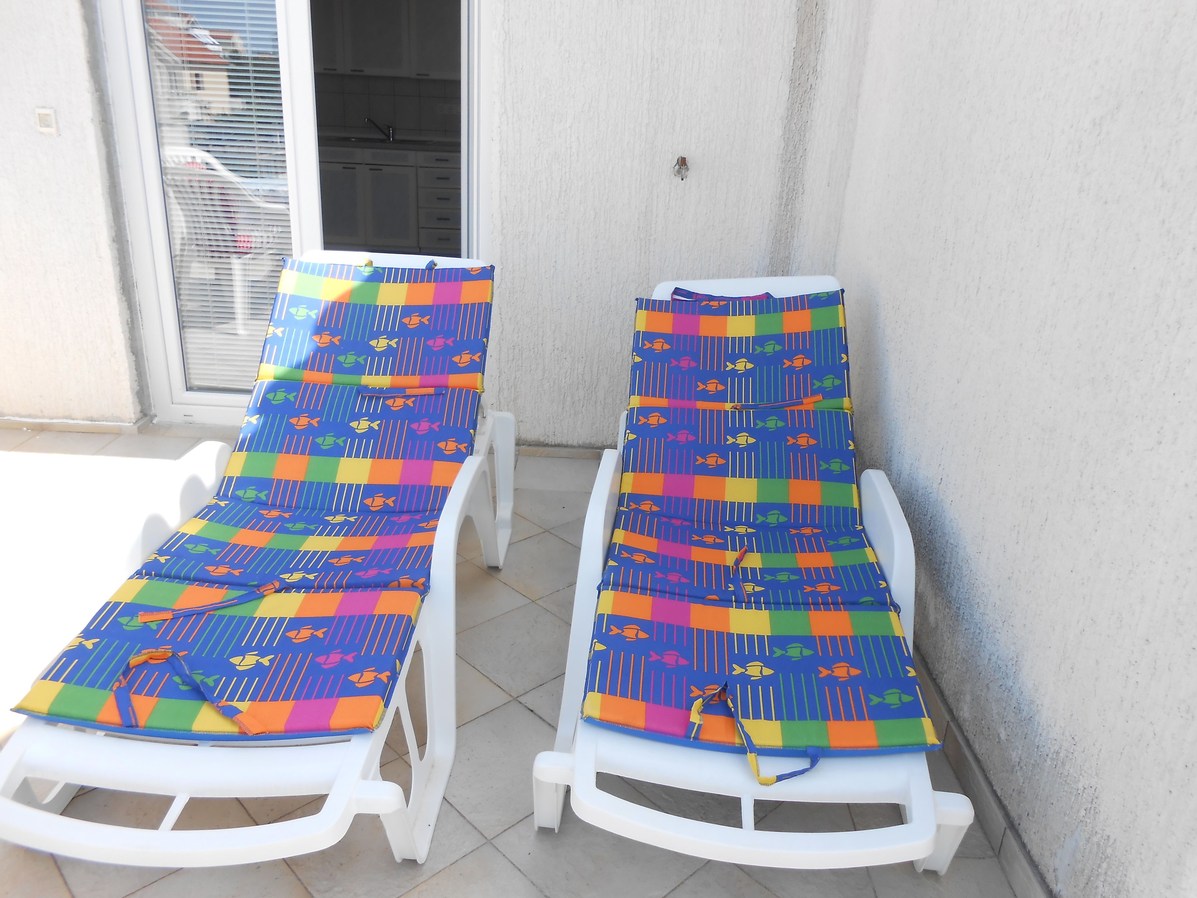 Two white lounge chairs with colorful fish-patterned cushions, positioned against a wall with a window and a door.