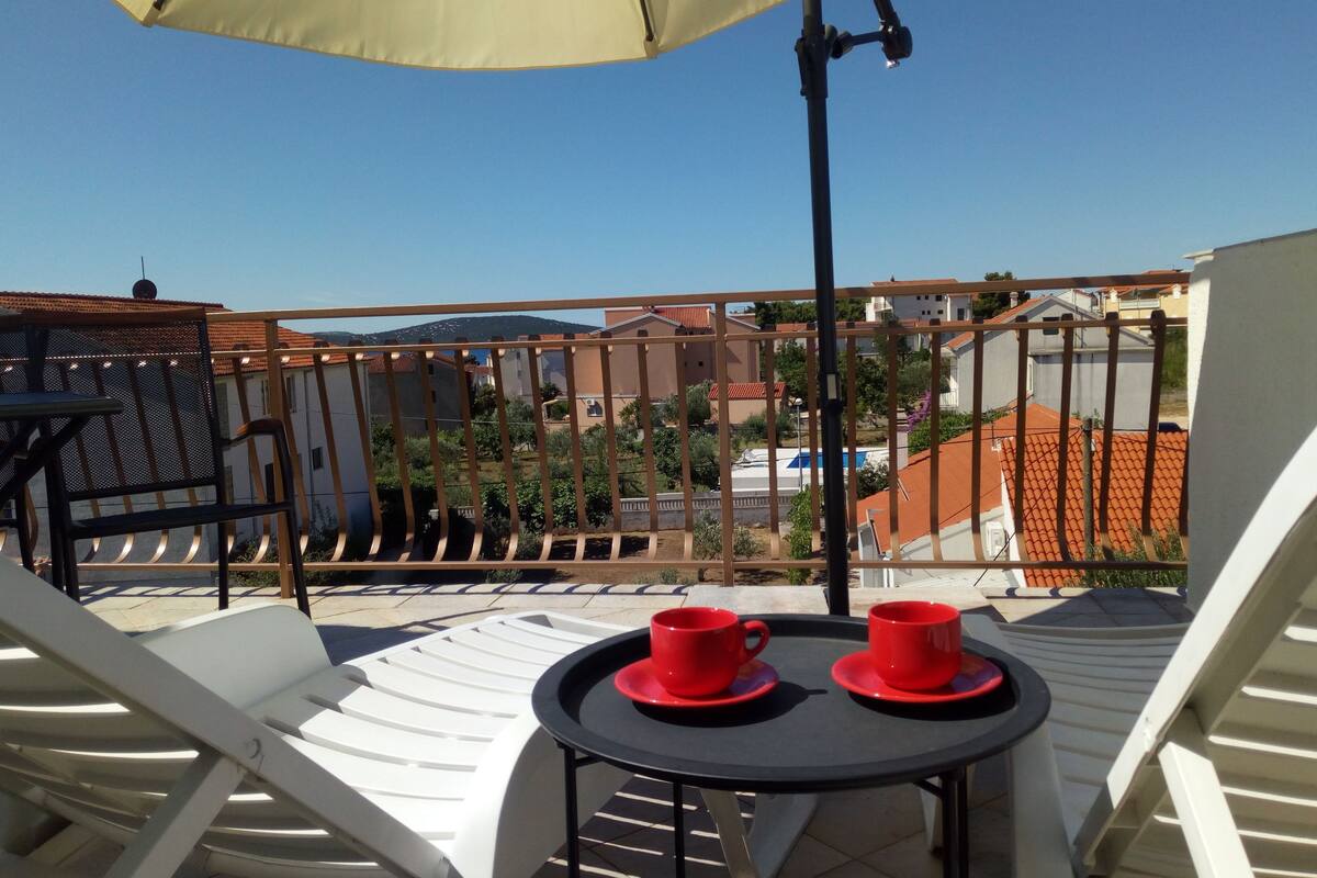 A balcony with white chairs, a table, and two red cups.