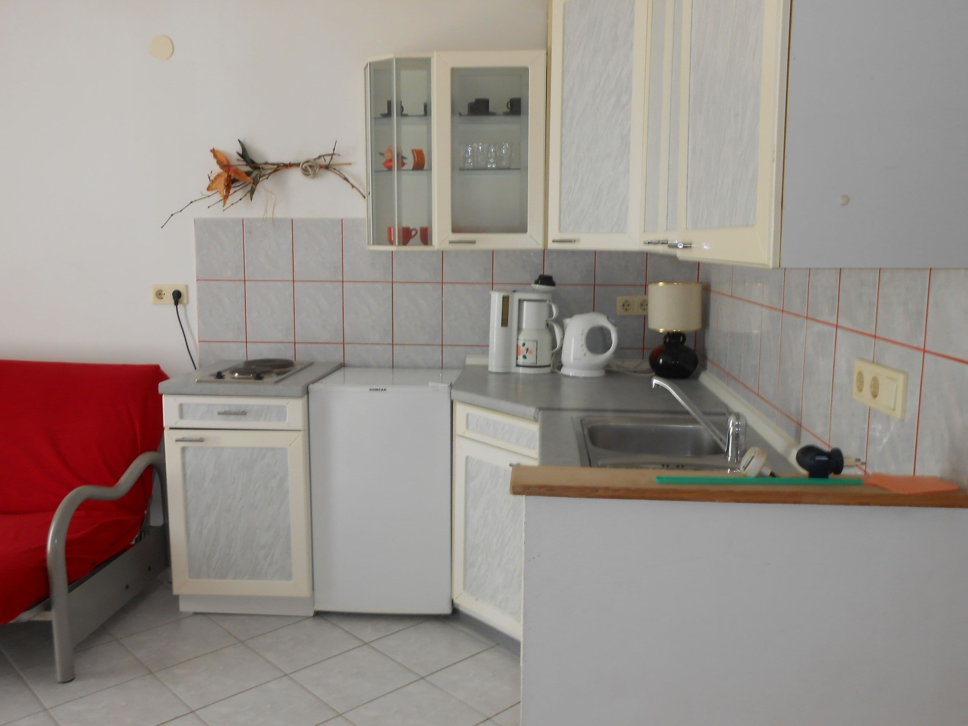 Una cucina compatta con mobili bianchi, un piccolo frigorifero, una macchina da caffè e un lavandino.