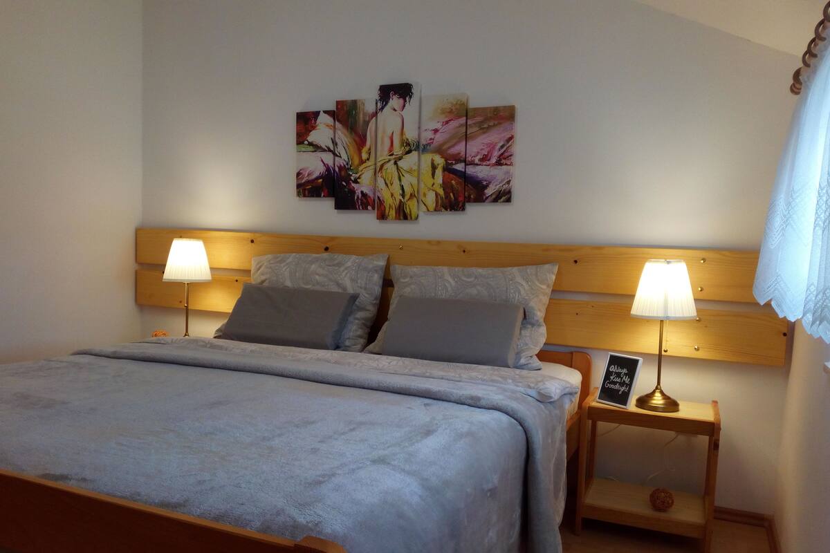 A neatly made bed with a wooden headboard, two bedside lamps, and a wall-mounted artwork above it.