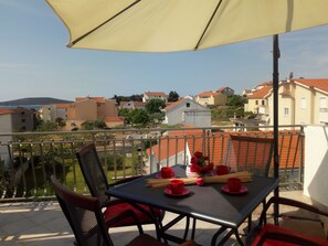 Een balkon met een tafel gedekt voor twee personen, rode bekers en een bloevas.