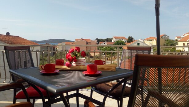 Une table avec des tasses rouges et un gâteau, placée sous un grand parasol sur une terrasse extérieure.