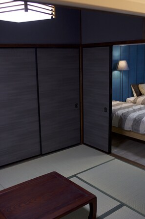 A room with tatami flooring, a wooden table, and a bed with a striped bedspread. - Lee106 Iida Accomodation (Iida)
