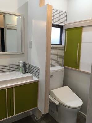 A compact bathroom with a white sink, green cabinets, a toilet, and a window above the toilet. - Lee106 Iida Accomodation (Iida)