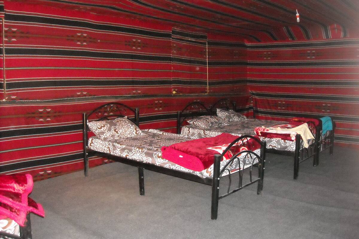A room with three beds, each with a patterned bedspread and pillows. The walls are adorned with red and black striped wallpaper.
