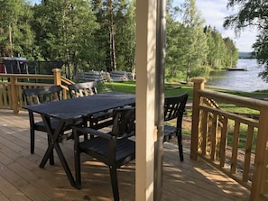 Une terrasse extérieure avec une table et des chaises, donnant sur un lac où l’on peut voir des bateaux et un quai.