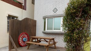 A wooden picnic table with a red wheelbarrow in front of a white brick building with a window and a decorative tile. - Yu Lei B&B (Huxi)