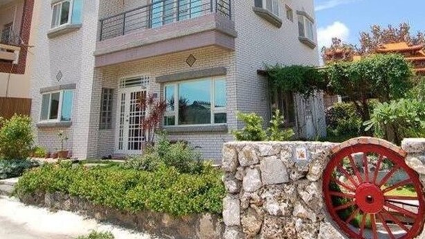 A two-story building with a balcony on the second floor, a stone wall in the foreground, and a red decorative wheel. - Yu Lei B&B (Huxi)