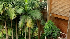 Un bâtiment en bois doté d’un balcon donnant sur un jardin luxuriant, avec des palmiers et une colline en arrière-plan.