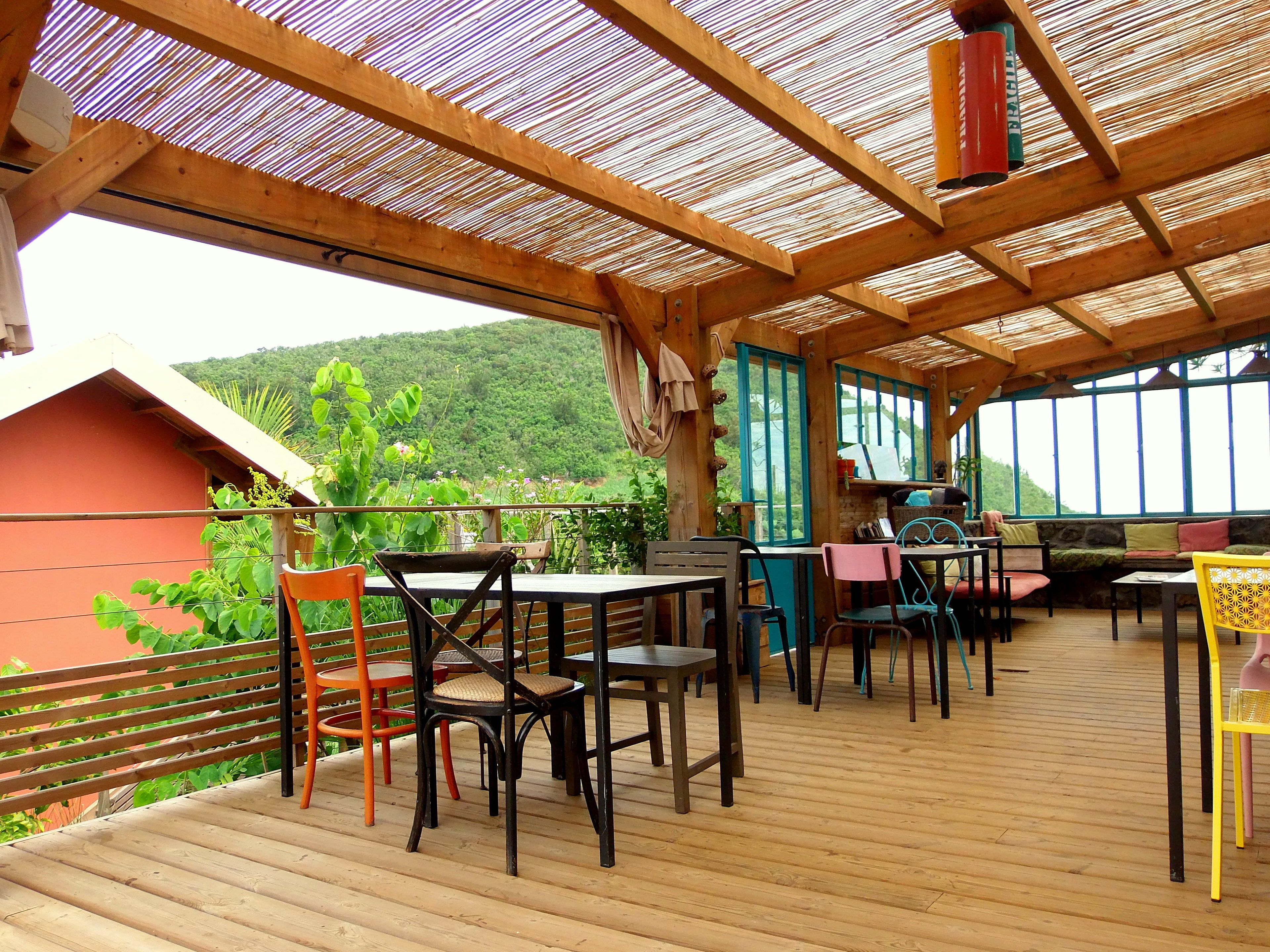 An outdoor wooden deck with tables and chairs, overlooking a lush green landscape.