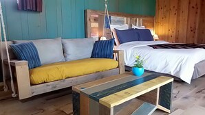 Une pièce chaleureuse avec un canapé en bois, un lit recouvert de draps blancs et une plante bleue dans un pot, posée sur une table en bois.