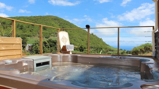 Un bain à remous avec une terrasse en bois et une vue sur une colline verdoyante et l’océan.