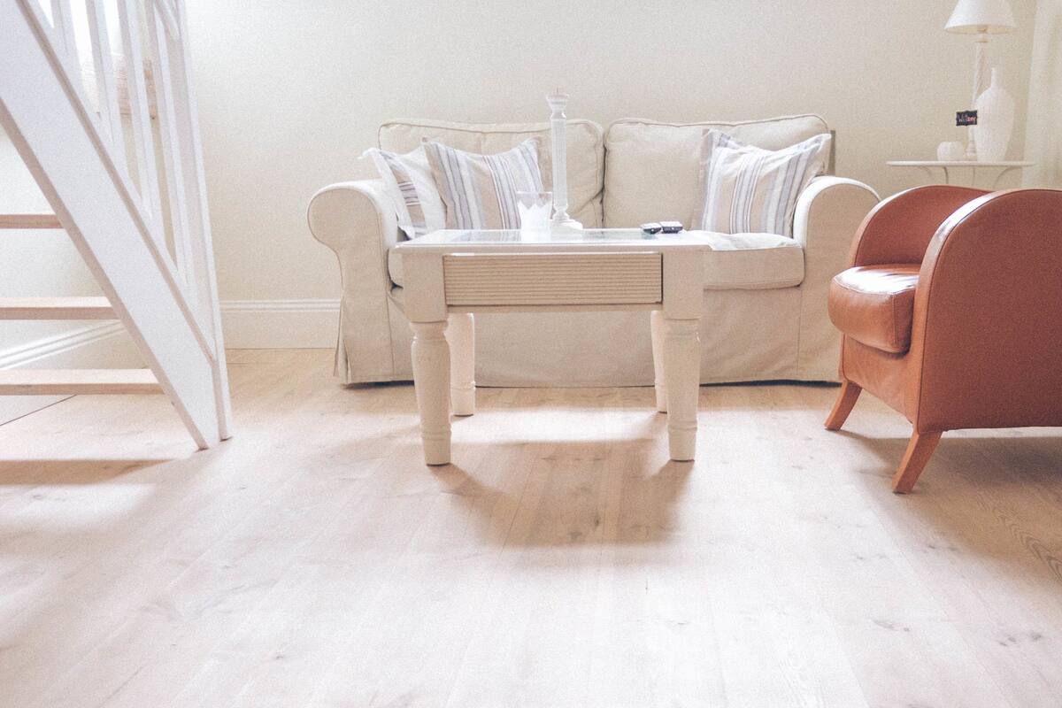 Una sala de estar con un sofá blanco, una mesa de centro de madera y un sillón marrón.