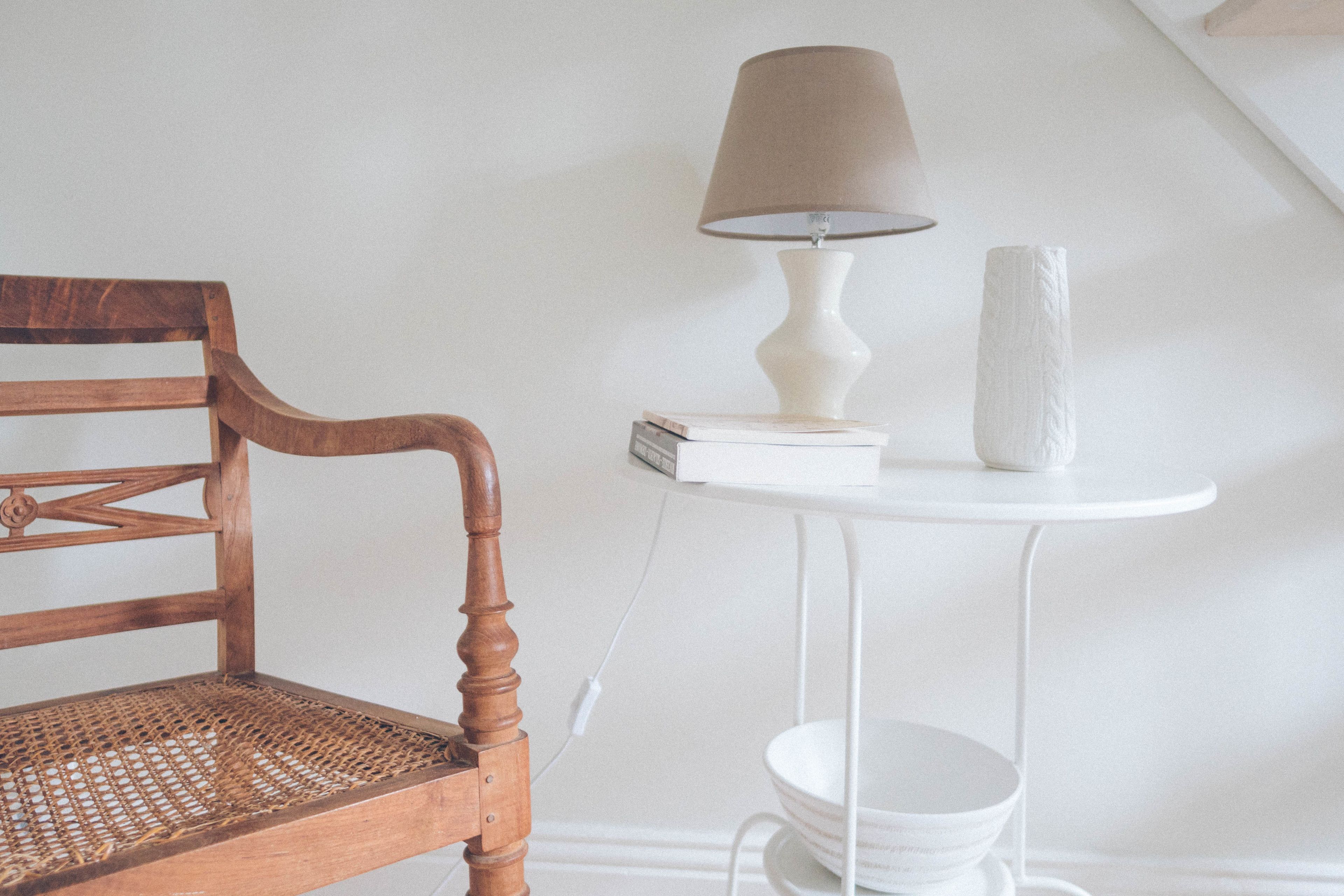 Une chaise en bois avec un siège en osier, une table blanche avec une lampe et un rouleau d’essuie-tout.