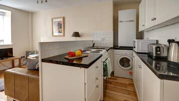 A compact kitchen with a stove, microwave, and washing machine. There is a small dining area with a table and a sofa.