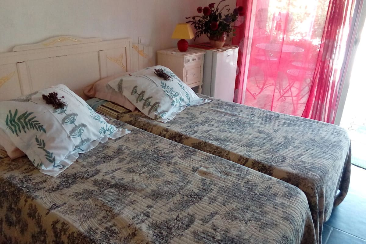 Een kamer met twee bedden, elk voorzien van beddengoed met bloemenprint en decoratieve kussens. Er staat een klein nachtkastje met een lamp en een bloevas.