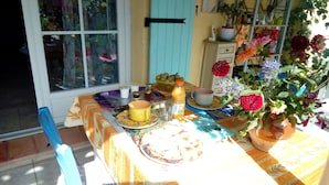 A dining table with a variety of items including a bowl of fruit, a bottle of juice, and several cups and plates. - B&B Chez Rose-Marie (Vaison-la-Romaine)