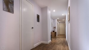 A hallway with white walls, wooden flooring, and recessed ceiling lights. There are doors on the left and a small table with a vase on the right. - Italianway Corso Lodi 121 (Milan)
