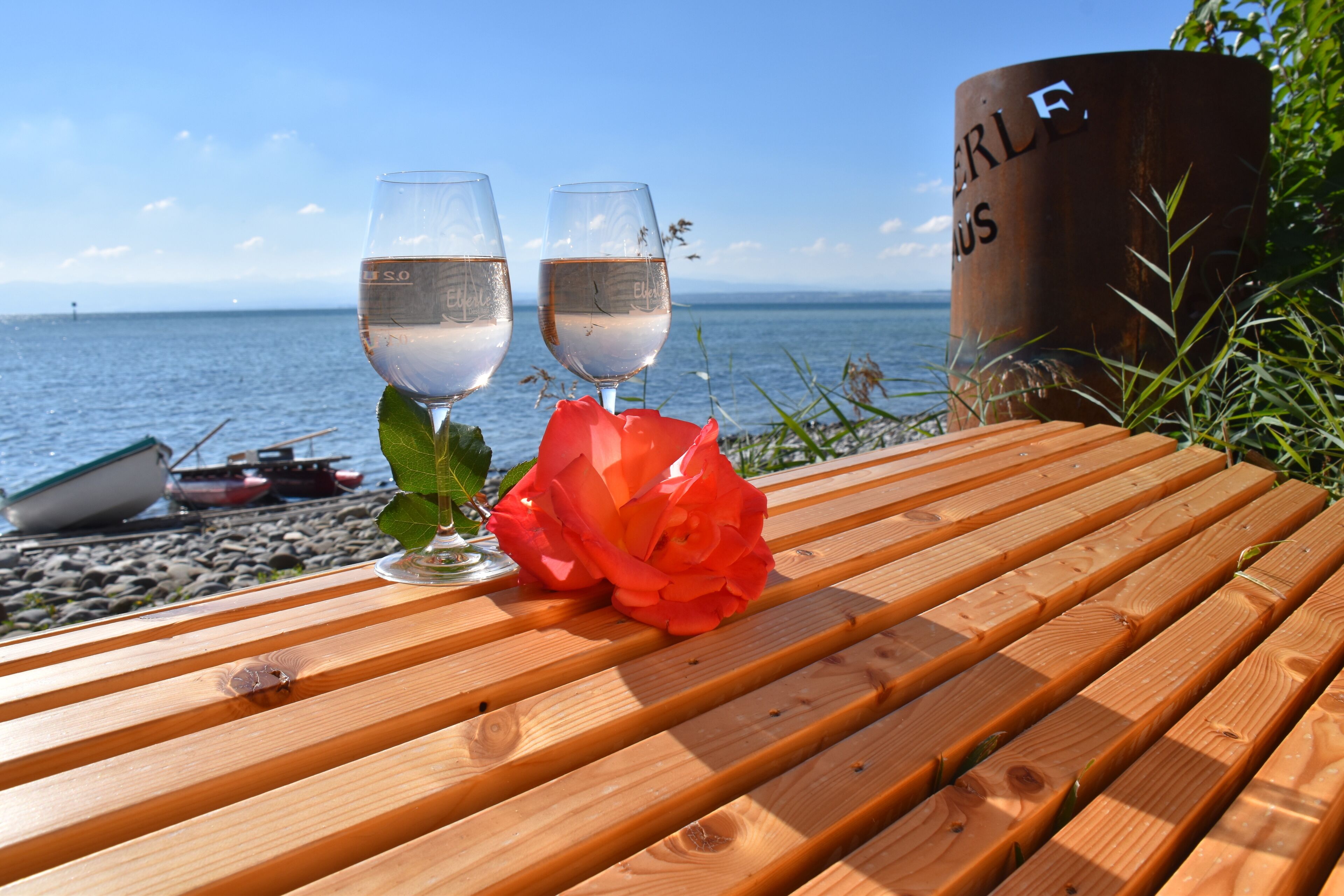 A wooden table with two glasses of white wine and a red rose.