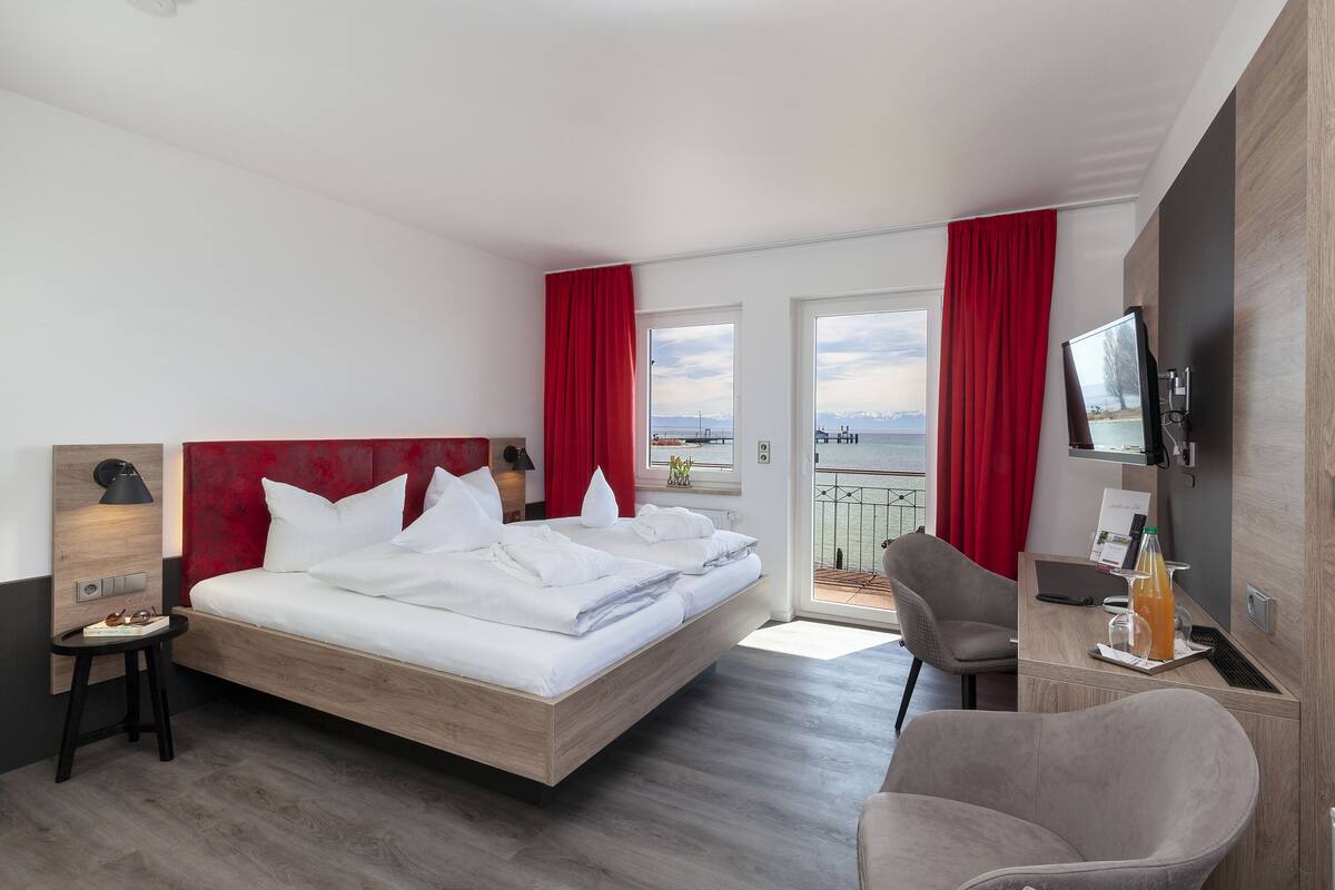 Habitación de hotel moderna con cama, escritorio, silla, televisor y balcón con cortinas rojas.