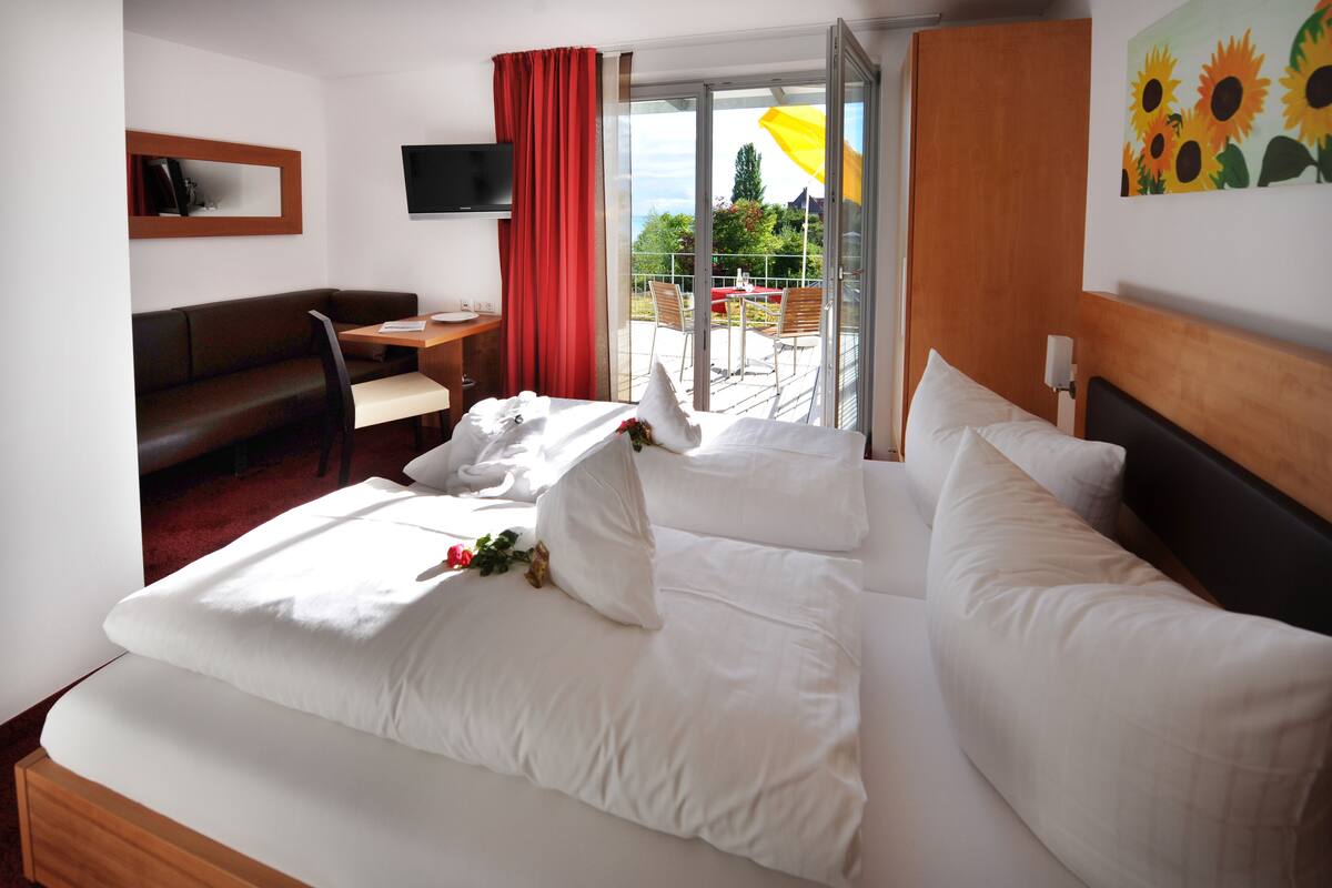 Habitación de hotel con cama, escritorio, silla, televisión y balcón con mesa y sillas.