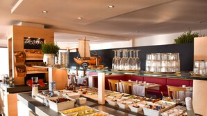 Un bufé con diversas opciones de comida y bebidas, entre ellas frutas, quesos y un adorno con forma de barco.