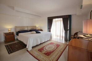 A hotel room with a bed, a desk, a chair, a nightstand, and a window with curtains. - Apartment/ flat - Taormina (Taormina)