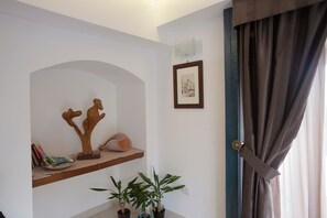 A room with a wooden shelf holding books and decorative items, a framed picture on the wall, and a door with a curtain. - Apartment/ flat - Taormina (Taormina)