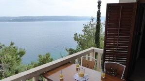 Une table en bois, entourée de chaises, sur un balcon donnant sur une étendue d’eau.